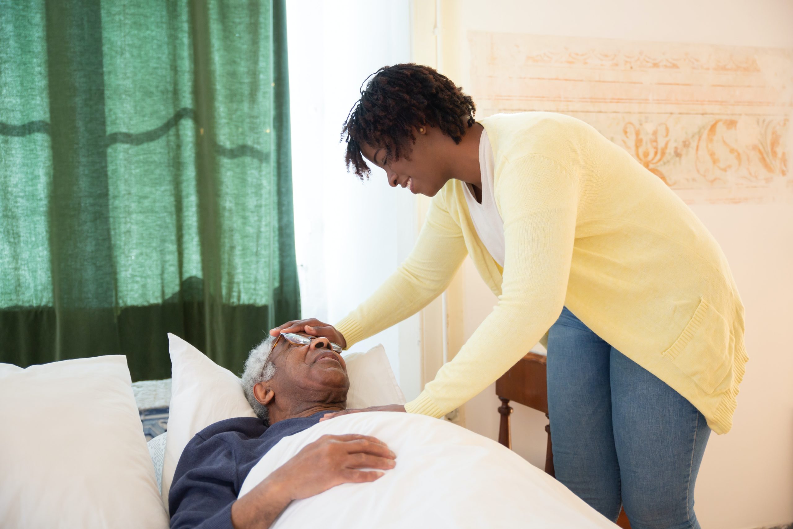 caregiver standing next to bed with older man laying down