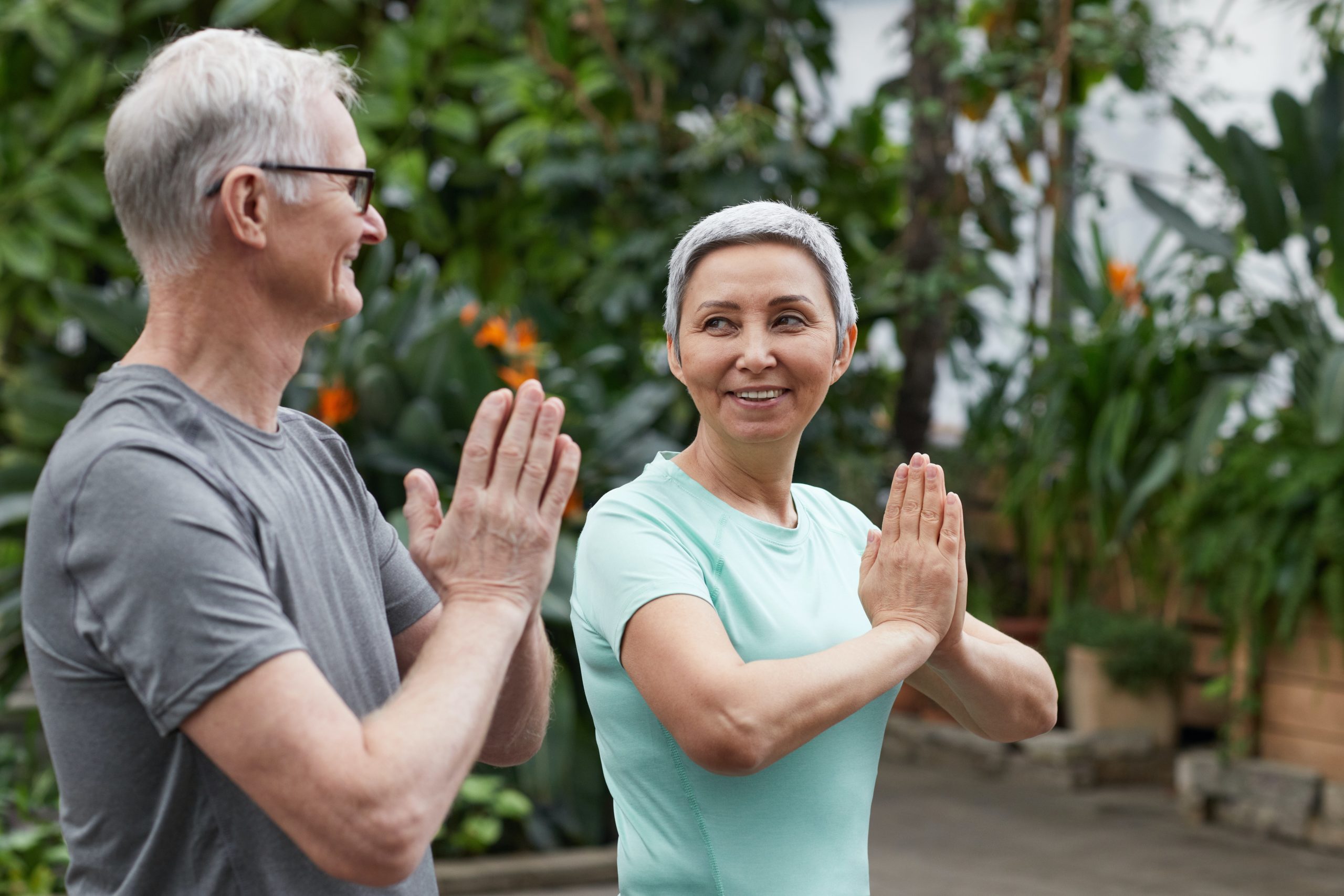 woman and man with grey hair smile and look at each other doing yoga
